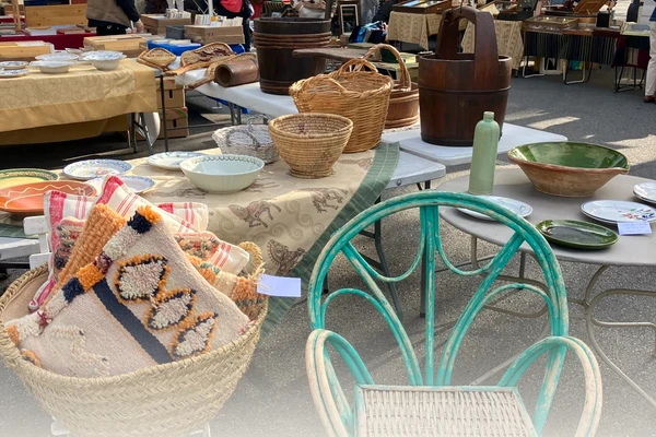 Flea market stalls with baskets, ceramics and a teal wicker chair